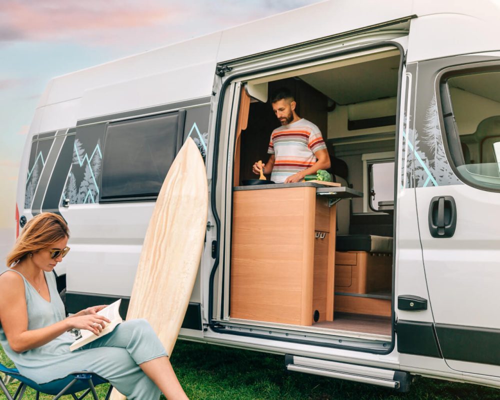 man-cooking-vegetables-in-a-camper-van-while-woman-FA8Q2L6